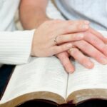 husband and wife hand on open bible