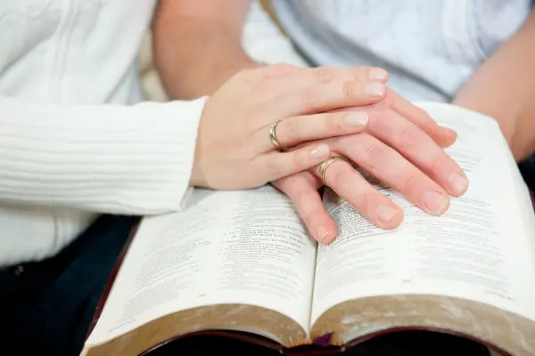 husband and wife hand on open bible