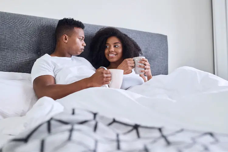happy black couple in bed sharing tea and tlaking